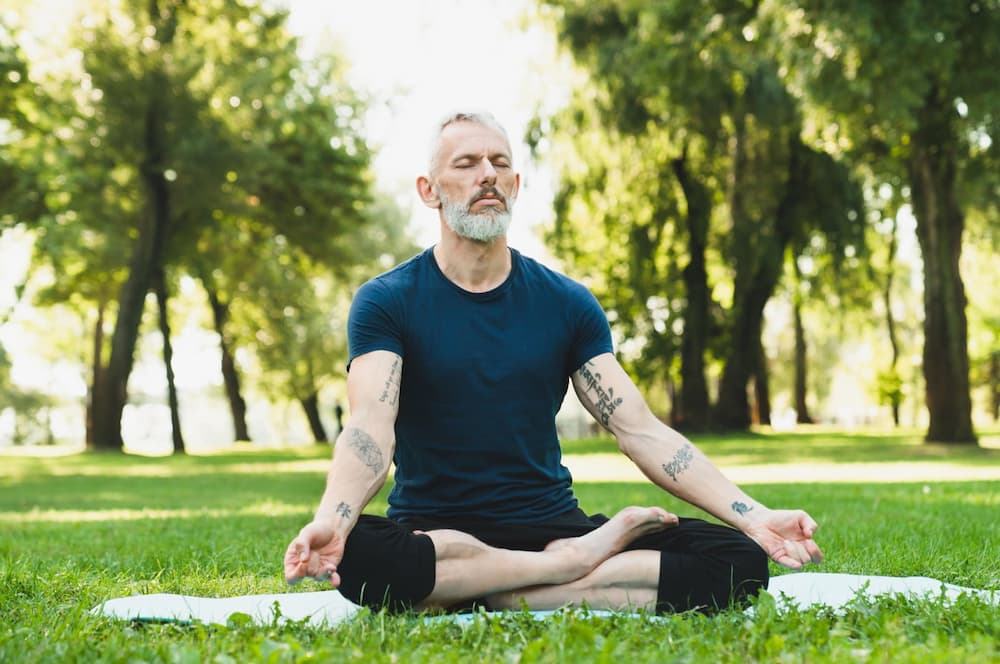 man-meditating-on-green-grass-yoga-mat-concentrati